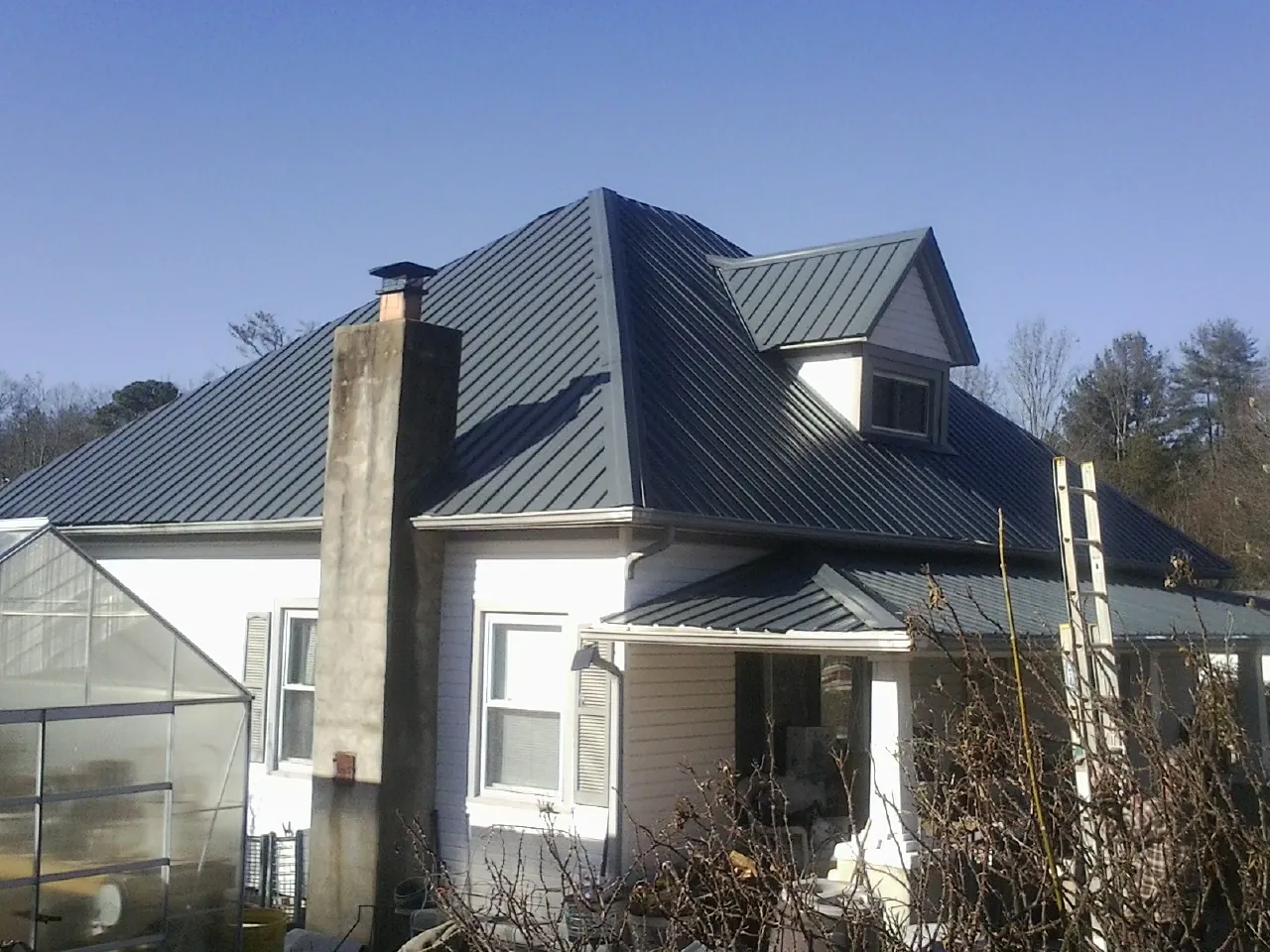 Dark blue standing seam metal roof on a white farmhouse with dormer — Slate & Tile Roof Repair by Roofing Brothers in Davison