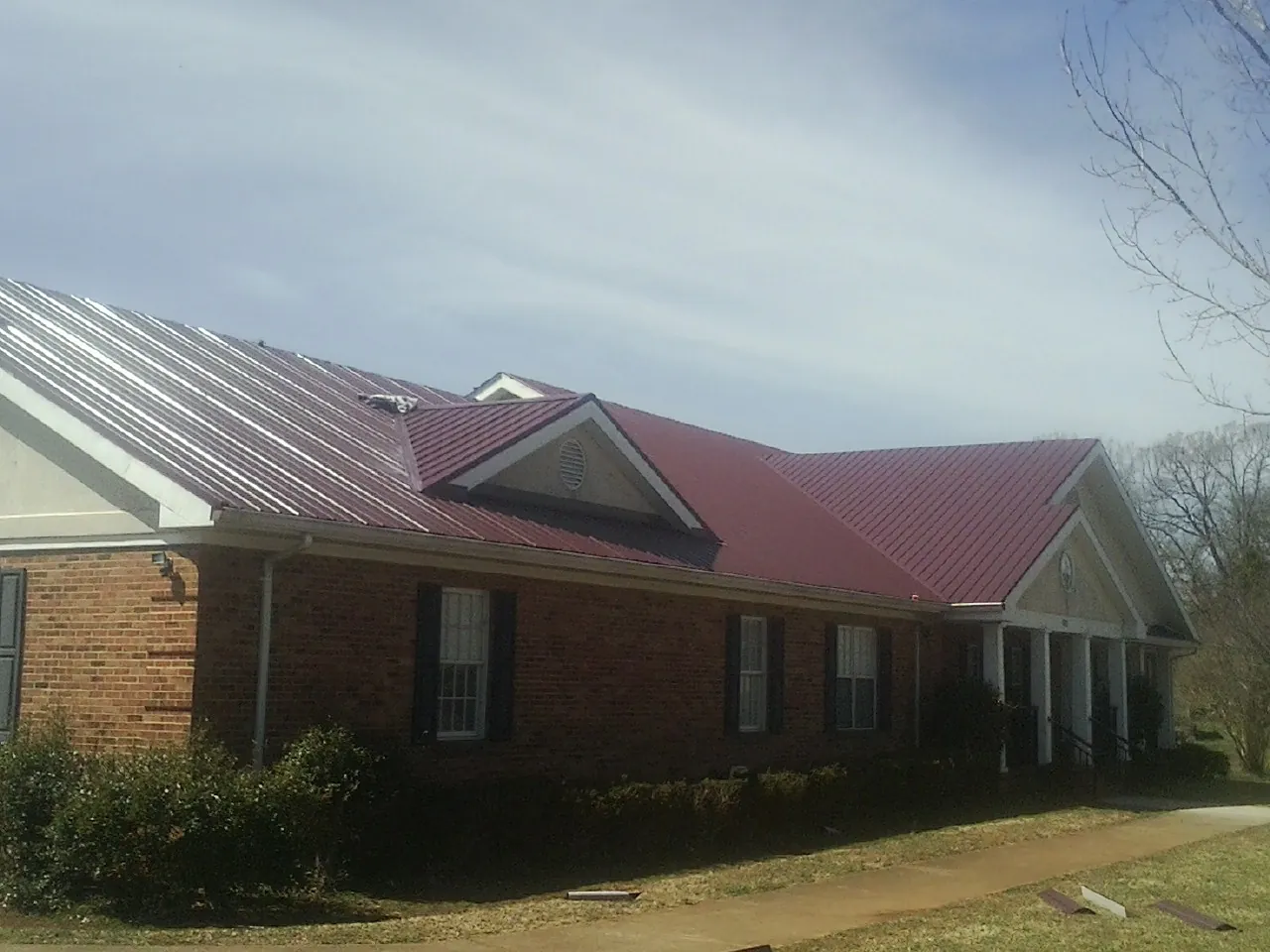 Red metal roof with gabled entries on a long brick building, from a Hail Damage Roof Repair job in Davison