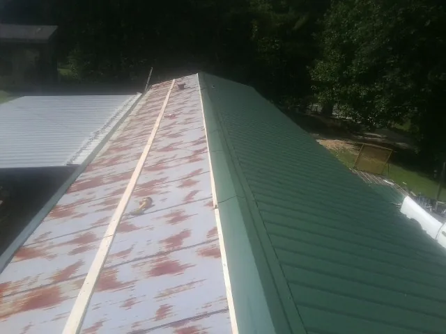 Old rusted panels beside newly installed green metal roofing — Wind Damage Roof Repair by Roofing Brothers in Davison