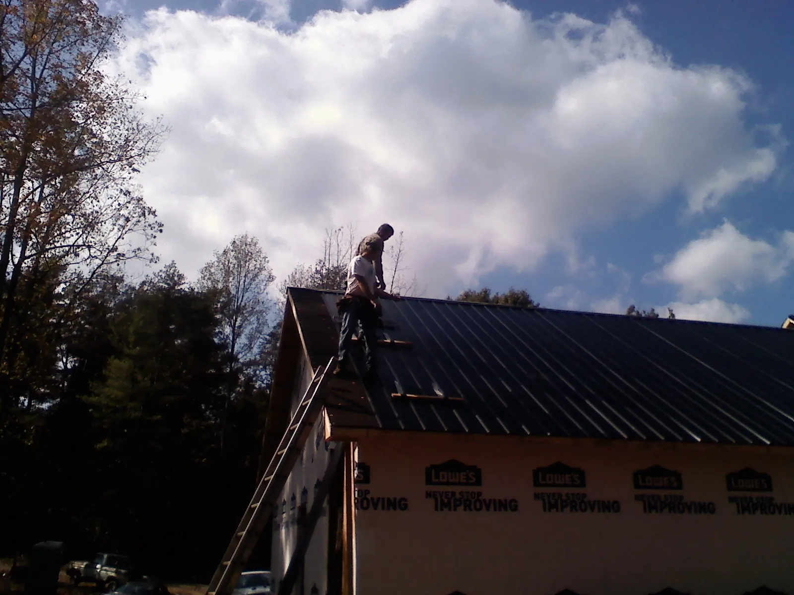 Roofer fastening dark metal panels high against a cloudy sky, from a Roof Inspection job in Davison