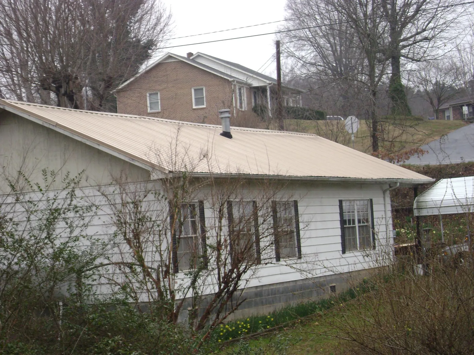 Tan metal roof on a white sided house set into a hillside — Commercial Roofing by Roofing Brothers in Davison