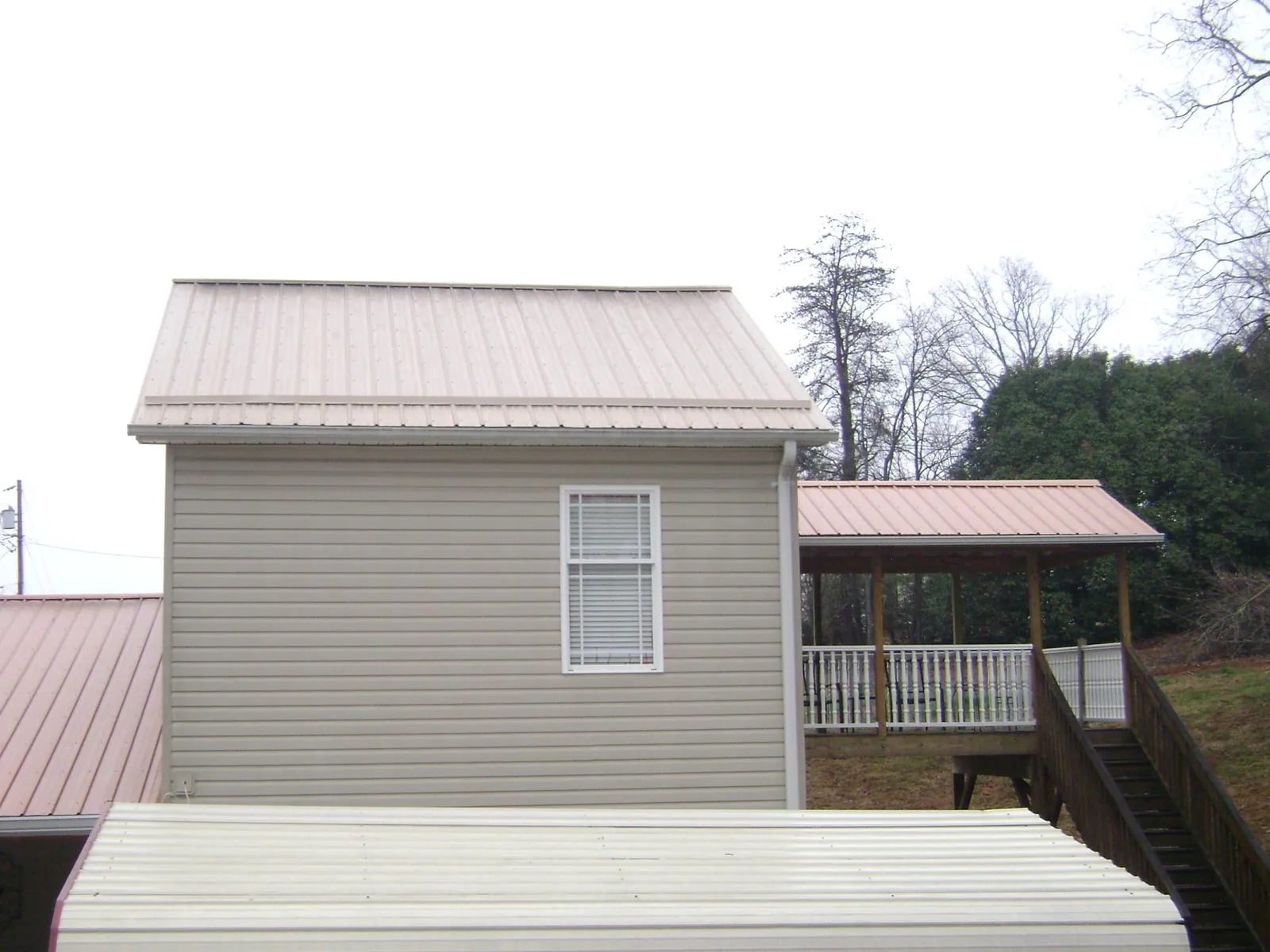 Tan metal roofs on a two story addition and attached porch, from a Roof Replacement job in Davison